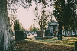 A person stands in a peaceful cemetery holding flowers in remembrance.