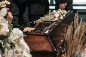 A poignant funeral moment with mourners gathered around a coffin decorated with flowers.
